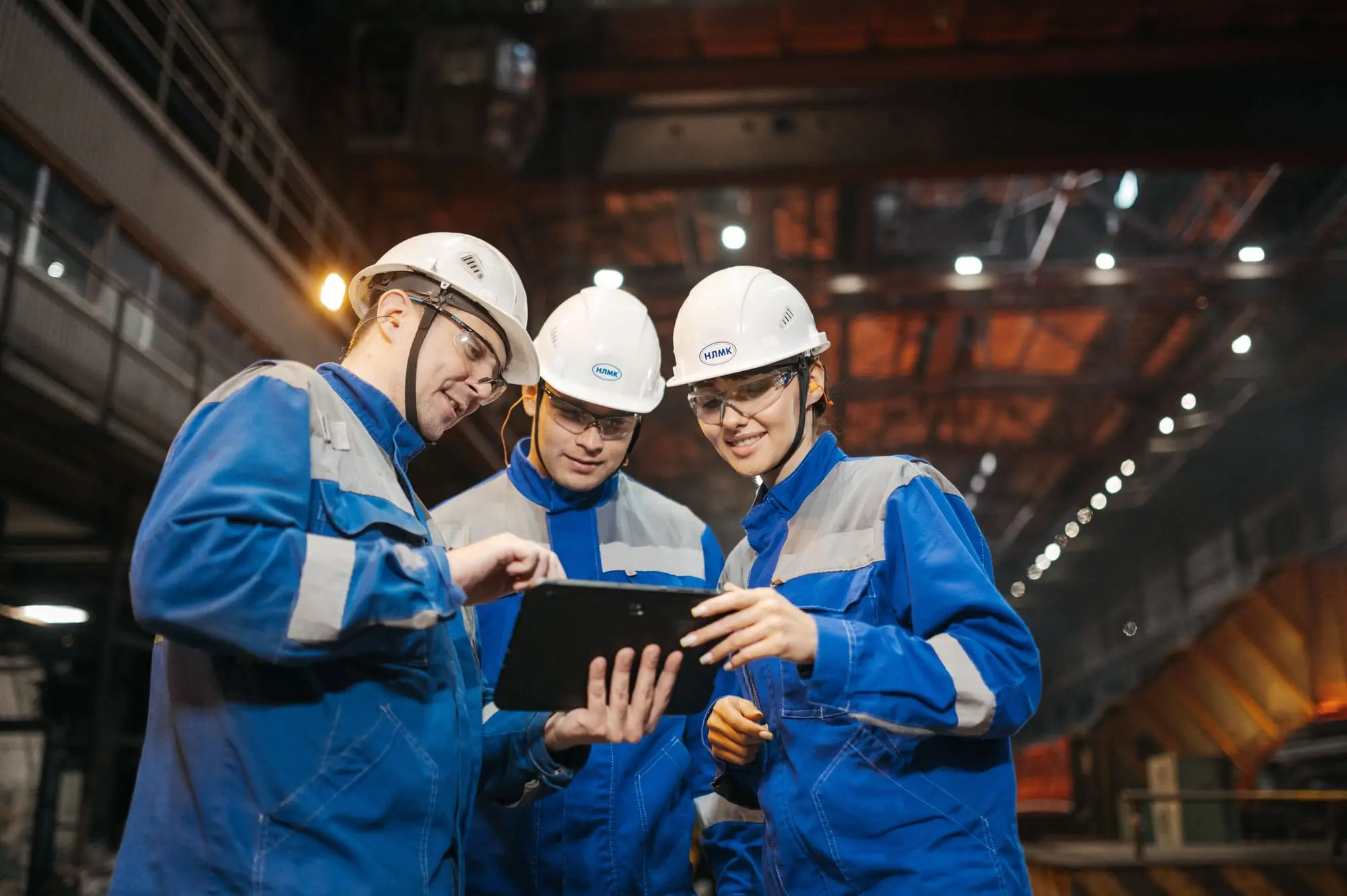 Baretli üç mühendis fabrikada tablet üzerinden teknik konuları inceliyor